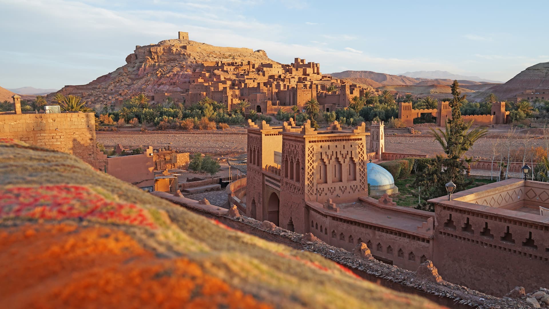 The earthen ksar of Aït Benhaddou climbing a hill, a crenellated kasbah in the foreground