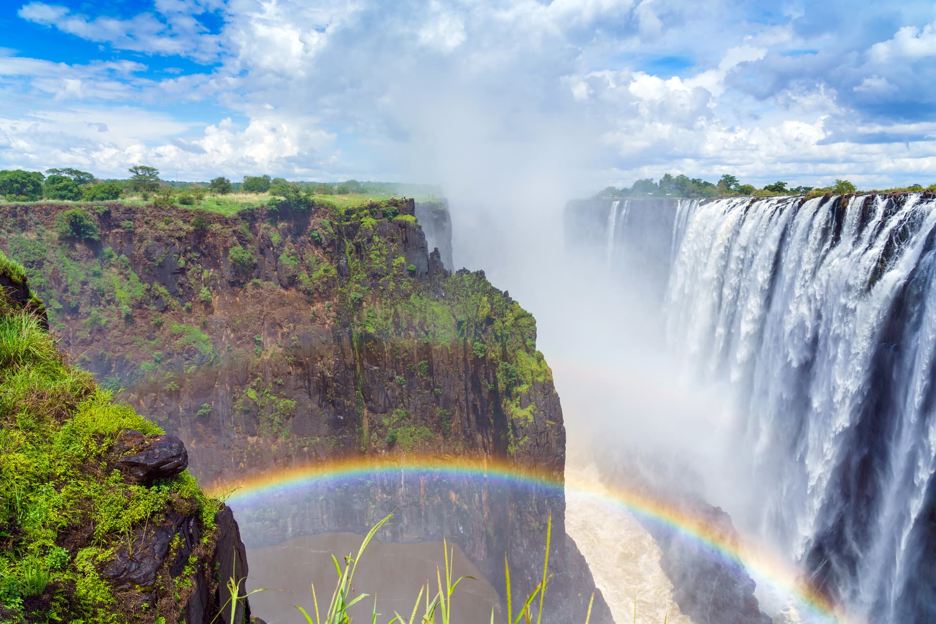 Victoria Falls plunging into a gorge, a rainbow in the spray under piled cloud